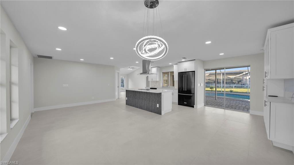 Image 2: Kitchen featuring white cabinetry, open floor plan, a kitchen island, high end black refrigerator, and range hood
