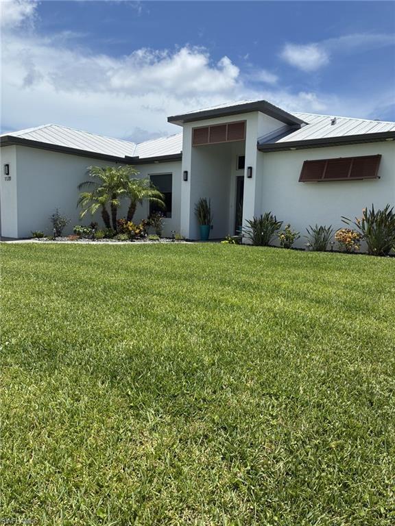 Image 3: Modern stucco exterior featuring a metal roof, prominent entry portico, decorative louvered window coverings, and established landscaping