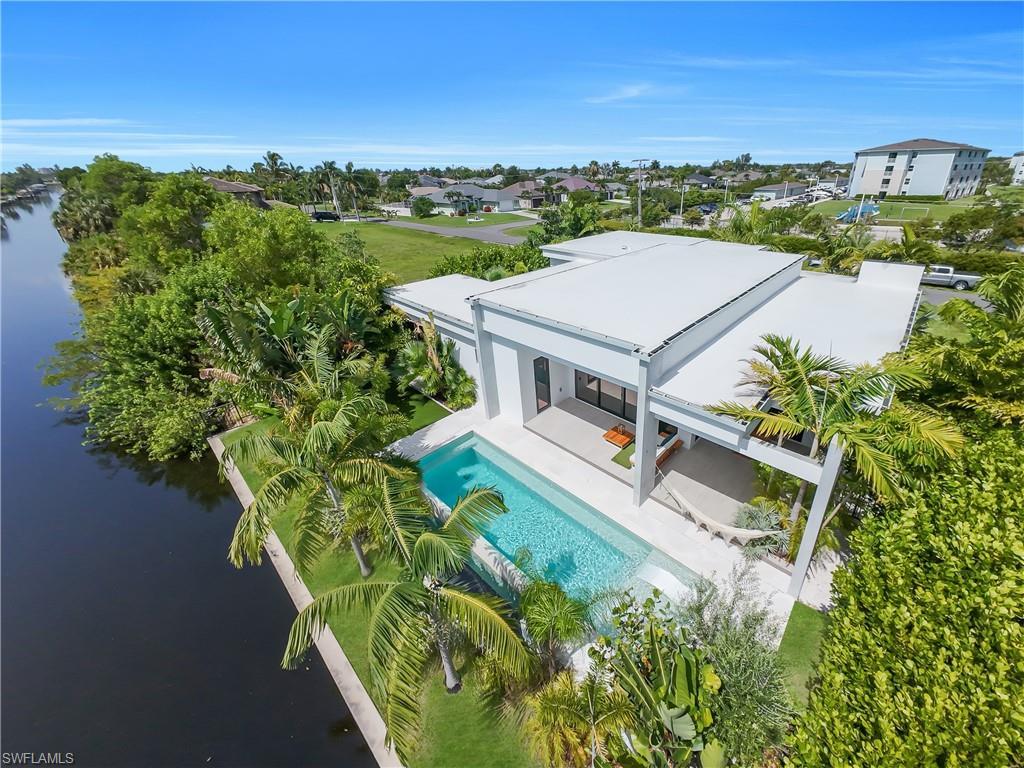 Image 4: Modern waterside residence featuring a rectangular pool, covered patio, lush tropical landscaping, and a flat roofline