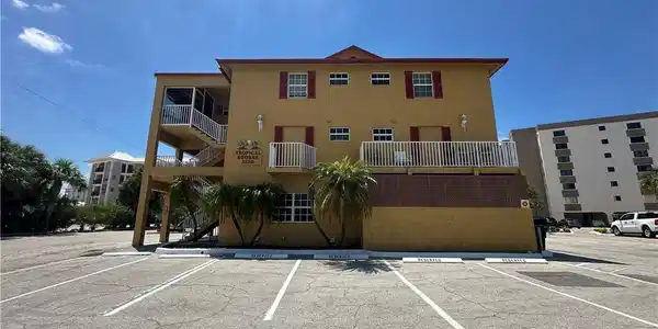 Image 3: Two-story building with a stucco exterior, exterior staircases, multiple balconies, and a paved parking area