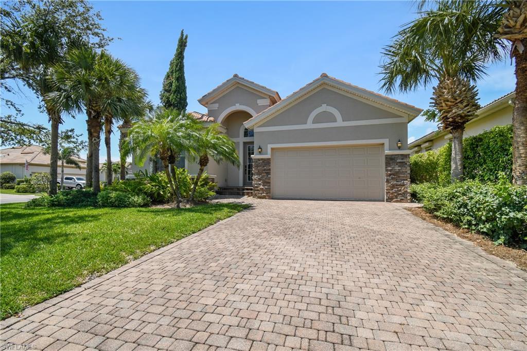 Image 2: Exterior featuring a paver driveway, stone accents, stucco facade, arched entryway, and tropical landscaping