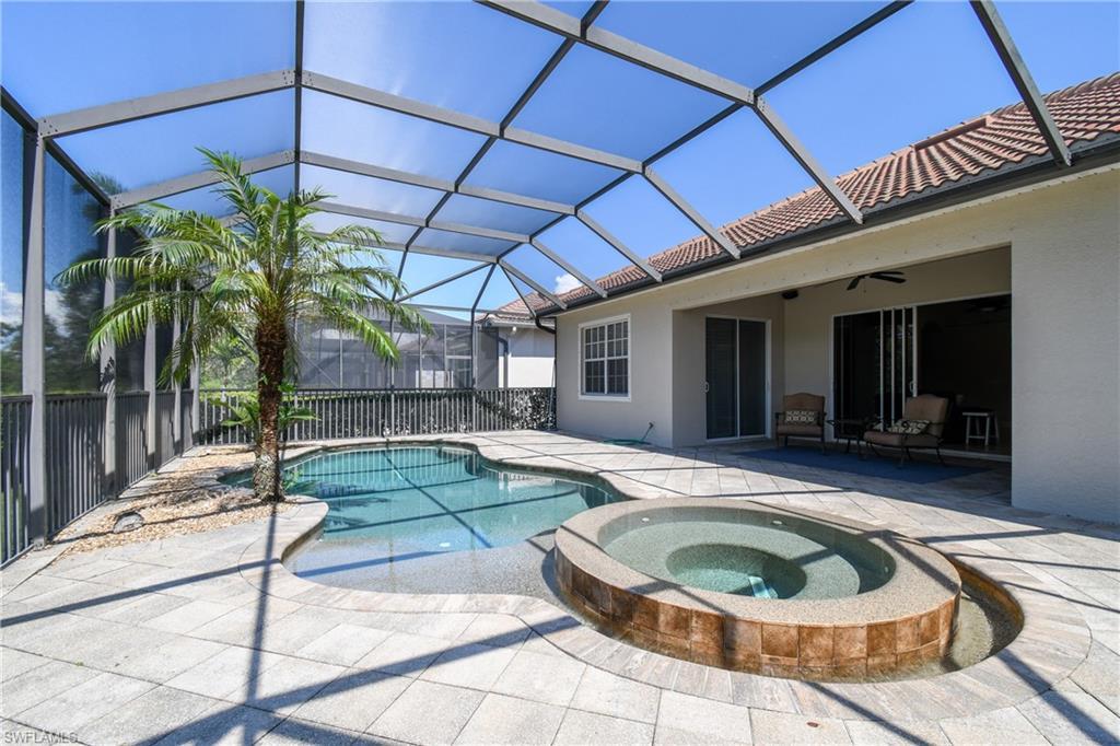 Image 3: Screened lanai featuring a freeform swimming pool, integrated spa with tile surround, and paver decking
