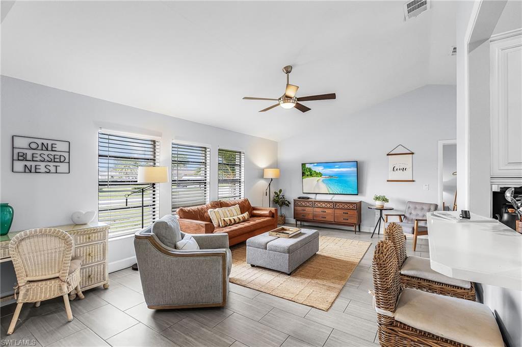 Image 2: Vaulted ceiling living area featuring tile flooring, ceiling fan, and multiple windows