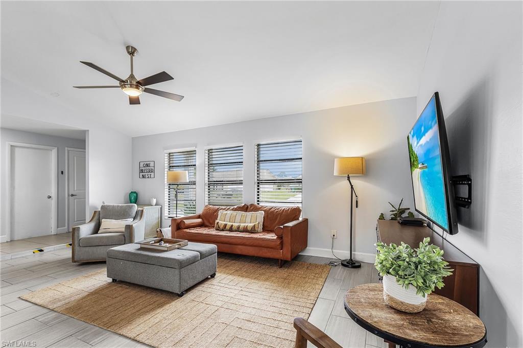 Image 4: Bright living area featuring wood-finish flooring, a contemporary ceiling fan, and multiple windows with blinds