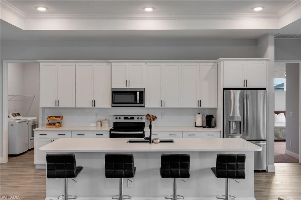 Image 2: Modern kitchen featuring white shaker cabinetry, stainless steel appliances, a center island with seating, a subway tile backsplash, and recessed lighting