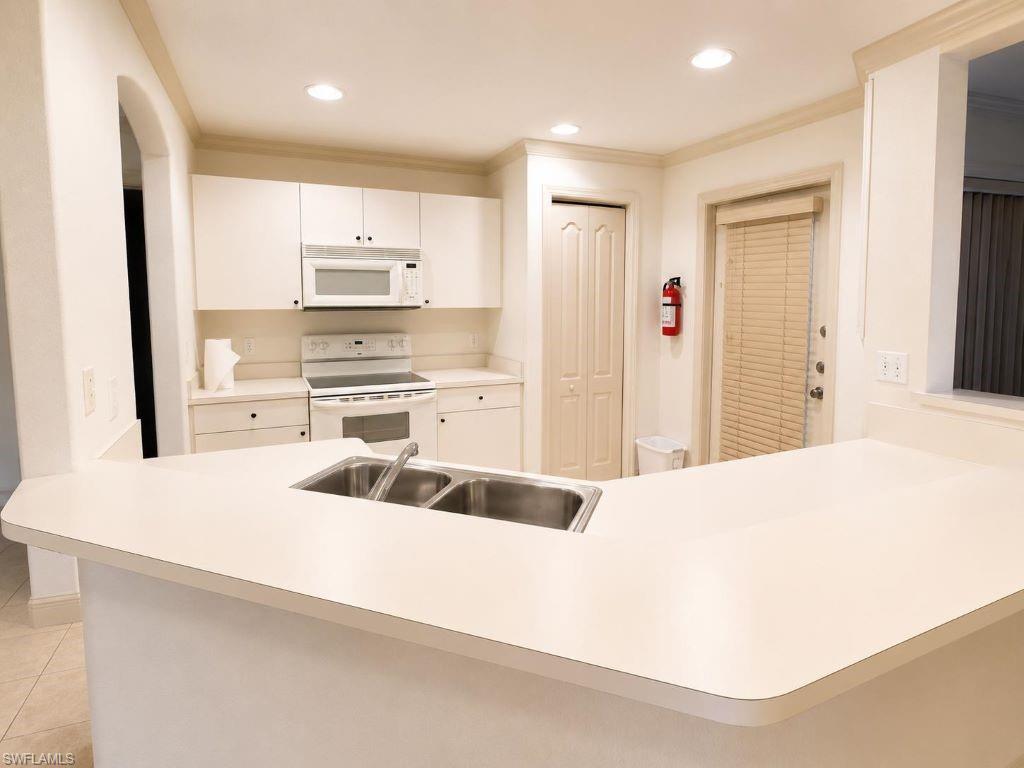 Image 4: Kitchen featuring an integrated breakfast bar with a double basin sink, white cabinetry with dark hardware, recessed lighting, and a full suite of white appliances including a range and microwave