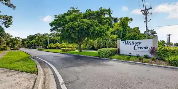 Image 3: Entry monument sign with raised lettering, surrounded by mature landscaping and a well-maintained asphalt road