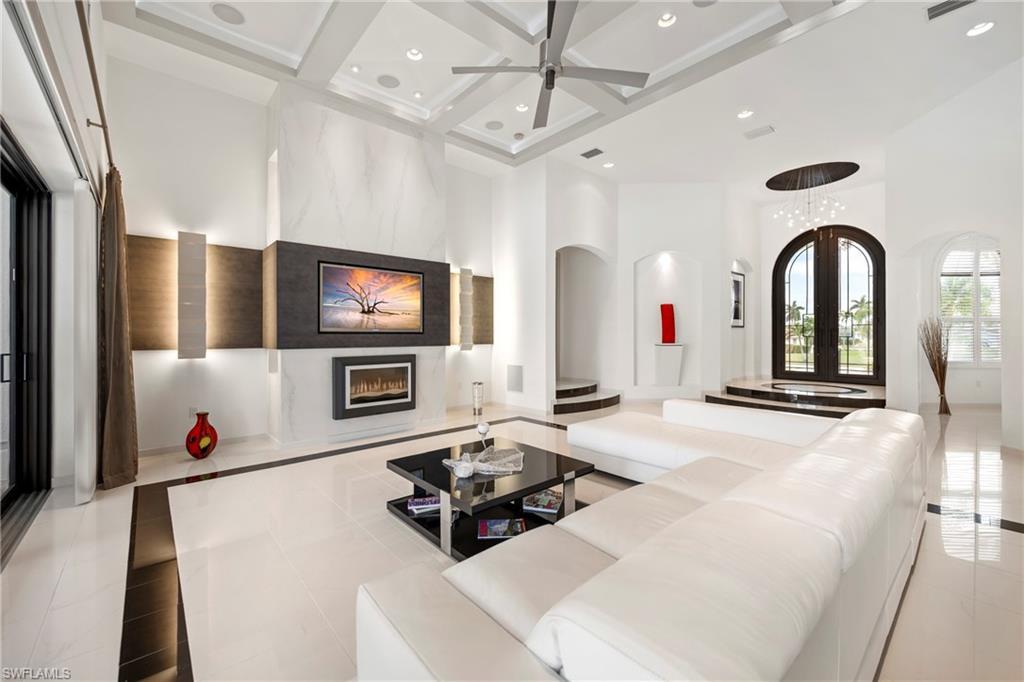 Image 4: Living area featuring a premium fireplace, coffered ceiling, ceiling fan, arched walkways, and inlaid floor details