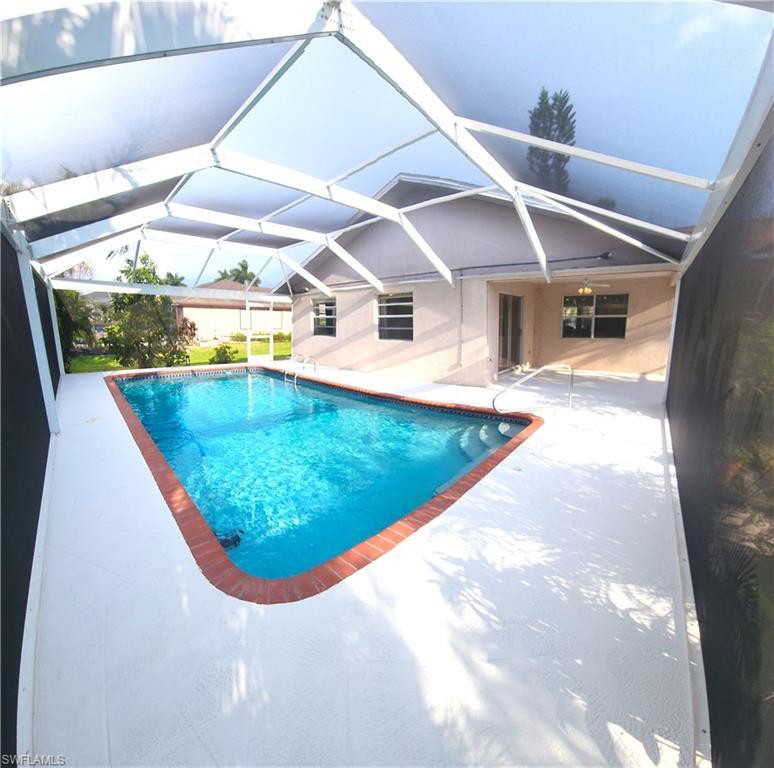 Image 2: Screened-in pool area featuring a rectangular pool with integrated steps, a brick coping, and a surrounding white deck