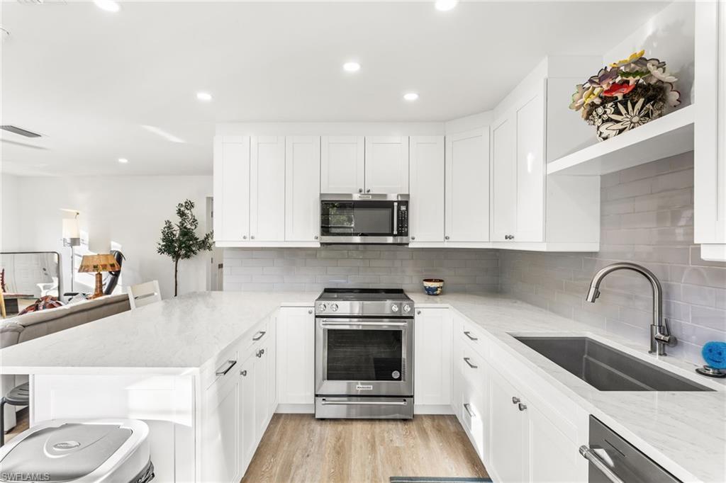Image 1: Kitchen featuring appliances with stainless steel finishes, light stone countertops, a breakfast bar area, white cabinets, and a peninsula