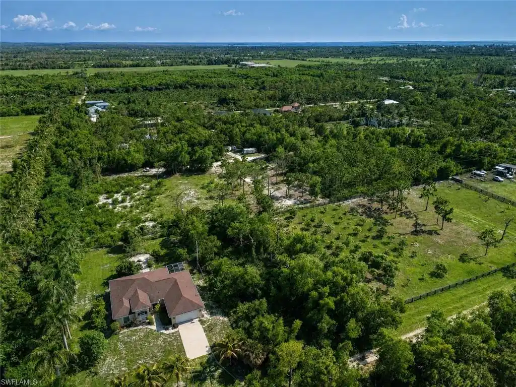 Image 1: Single-story residence set amidst expansive green acreage, featuring a brown shingle roof, attached garage, and a concrete driveway