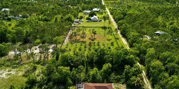 Image 4: Expansive aerial perspective showcasing a property with a distinct red-tiled roof and a light-colored driveway