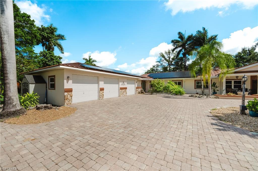 Image 2: View of front facade featuring stucco siding, stone siding, roof mounted solar panels, and decorative driveway