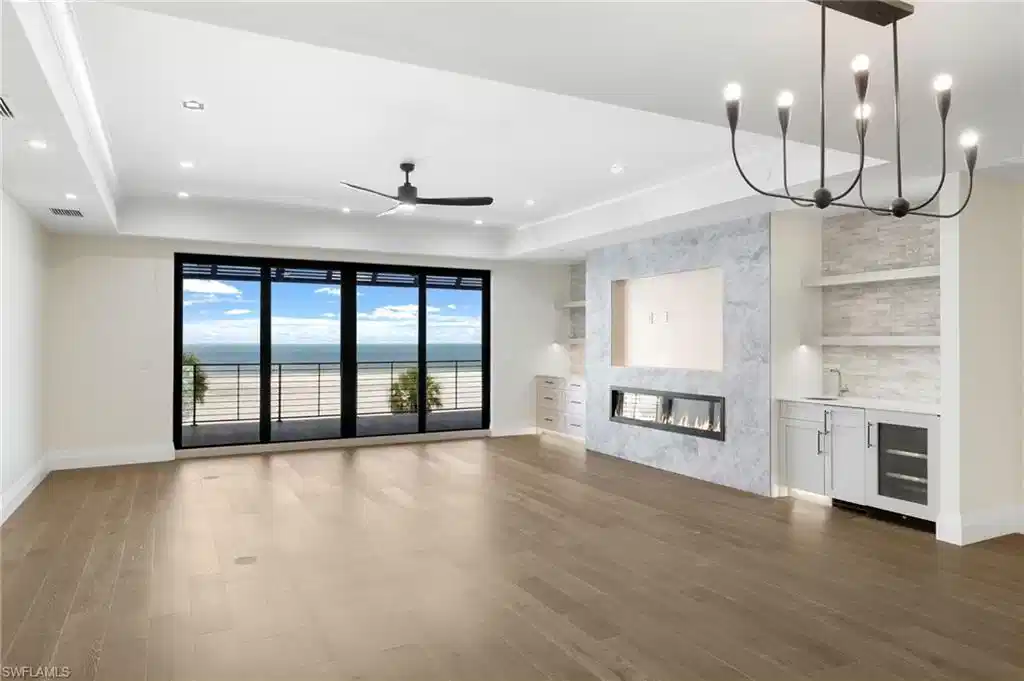 Image 1: Expansive sliding glass doors, wood-finish flooring, linear fireplace, integrated wet bar with beverage cooler, and recessed lighting
