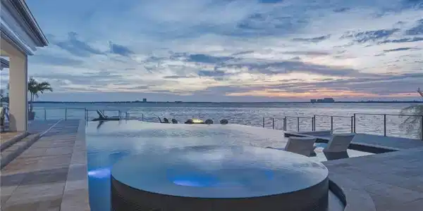 Image 4: Your private compound offers an unparalleled sense of seclusion, where a spectacular three-sided infinity pool&mdash;one of the only of its kind in Fort Myers&mdash;seamlessly frames the waterfront beyond. An inviting eight-person spa beckons, creating the perfect setting to unwind and indulge in serene relaxation after a day on the links.