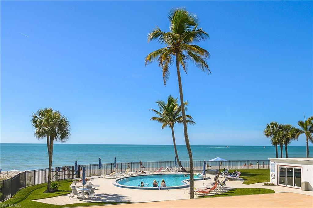 Image 2: Embassy Club pool featuring a relaxing patio area, gated beach access, a water view, and a fenced backyard