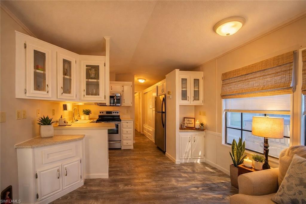 Image 4: Kitchen with glass fronted cabinets, white cabinetry, light countertops, stainless steel appliances, and dark wood-style floors