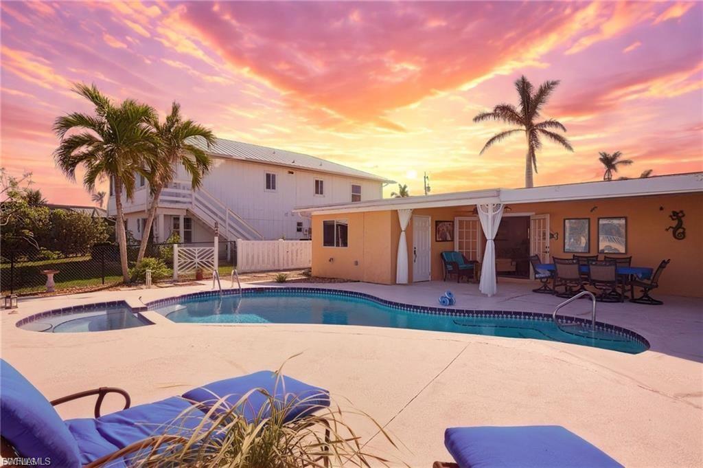 Image 2: Outdoor living space featuring a freeform swimming pool with integrated spa, expansive concrete patio, and a stucco-finish home exterior with French doors