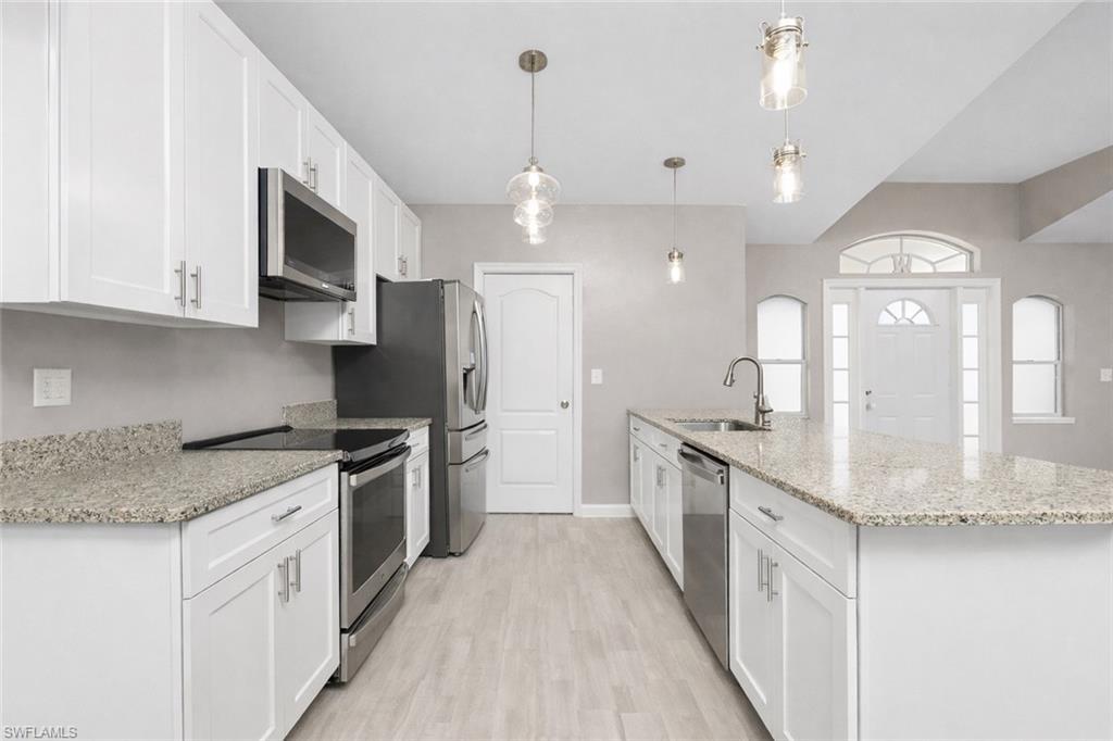 Image 4: Kitchen with stainless steel appliances, white cabinetry, light stone countertops, light wood-style flooring, and hanging light fixtures