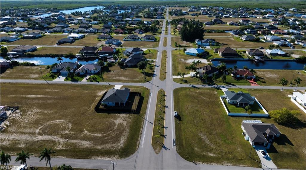 Image 3: Expansive aerial capturing multiple single-story residences with diverse architectural styles, featuring paved roadways, individual driveways, and partially developed lots