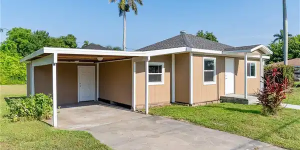 Image 2: View of front of property featuring a front lawn, an attached carport, concrete driveway, and a shingled roof
