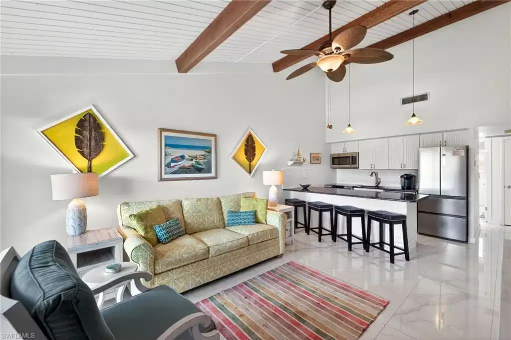 Image 1: Open-concept living area featuring a vaulted ceiling with exposed wood beams, white wood-finish ceiling panels, and large format tile flooring