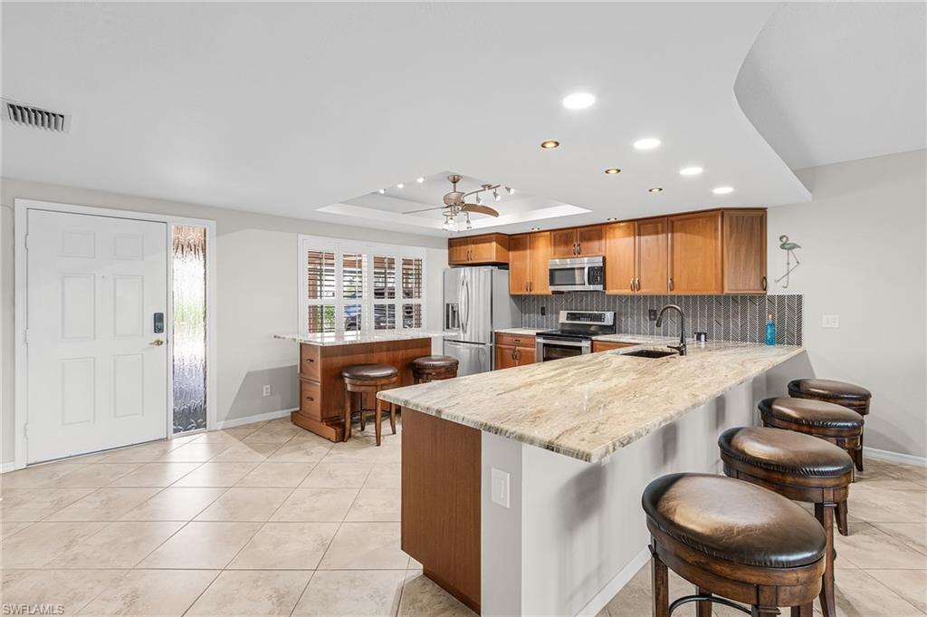 Image 3: Kitchen with a breakfast bar area, brown cabinets, a peninsula, a tray ceiling, and recessed lighting
