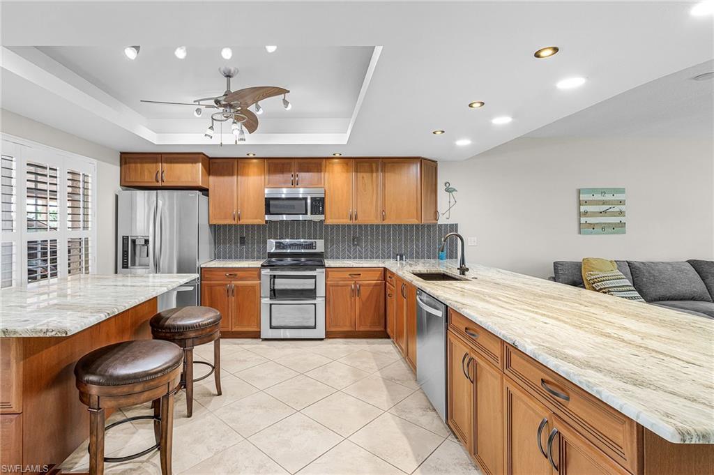 Image 4: Kitchen featuring a breakfast bar area, brown cabinetry, light stone counters, stainless steel appliances, and recessed lighting