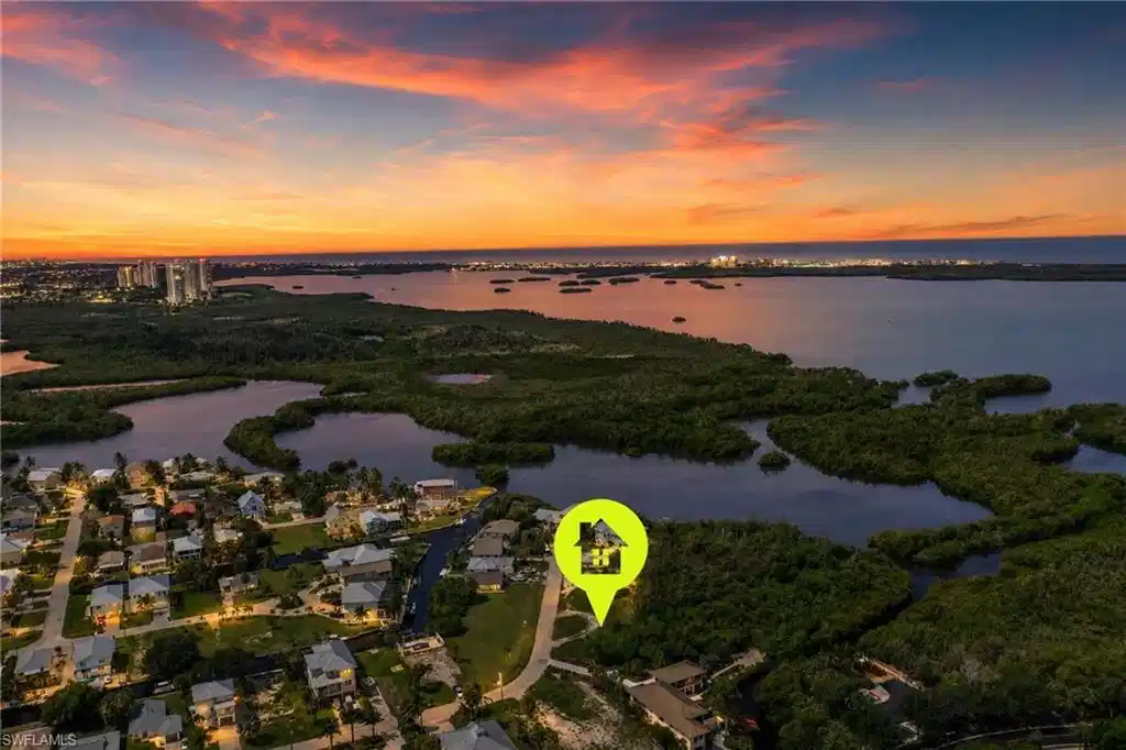 Image 1: Aerial perspective with waterfrontage, featuring residential properties, lush green landscaping, and distant urban lights under a colorful sky