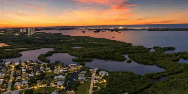 Image 2: Waterfront community with canal access, surrounded by diverse vegetation, and illuminated by a vibrant sunset backdrop
