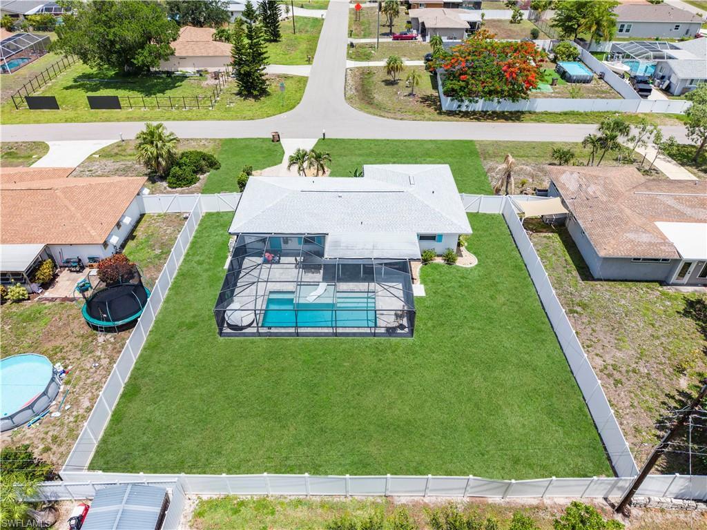 Image 2: Single-story residence featuring a screened-in swimming pool, manicured lawn, and white privacy fencing