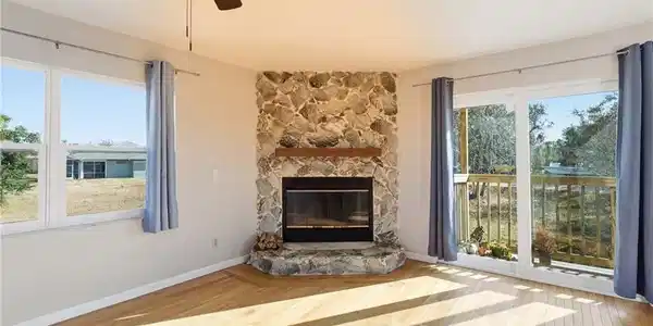 Image 3: Unfurnished living room with light wood-style floors, a ceiling fan, a stone fireplace, and healthy amount of natural light