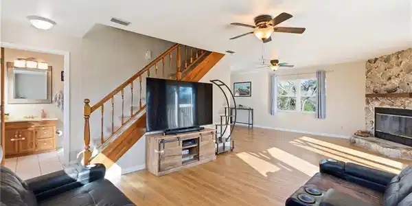 Image 4: Living area with ceiling fan, light wood-type flooring, and a stone fireplace