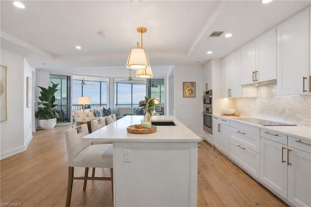 Image 1: Kitchen featuring white cabinetry, open floor plan, pendant lighting, a center island with sink, and a breakfast bar area - Virtually Edited Image