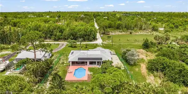 Image 2: Aerial perspective showcasing the property's exterior, featuring a swimming pool, a surrounding paved patio, and a fenced yard