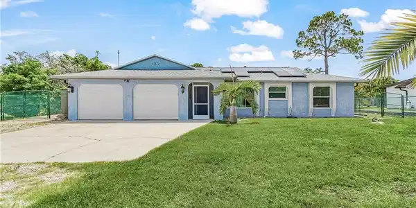 Image 3: Front exterior featuring a light blue stucco finish, a two-car garage, and solar panels
