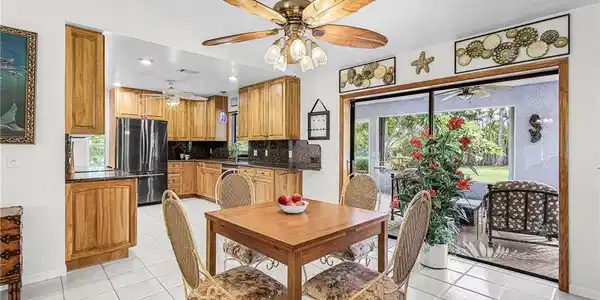 Image 4: Open-concept kitchen and dining area featuring wood cabinetry, dark granite countertops, and stainless steel appliances