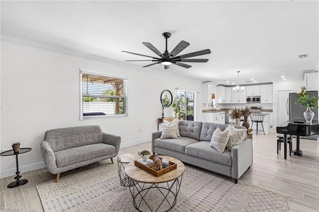 Image 4: Open-concept living space featuring light-toned wood-finish flooring, a contemporary ceiling fan, and white crown molding