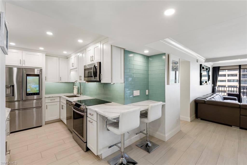 Image 3: Kitchen with appliances with stainless steel finishes, white cabinetry, and a kitchen breakfast bar