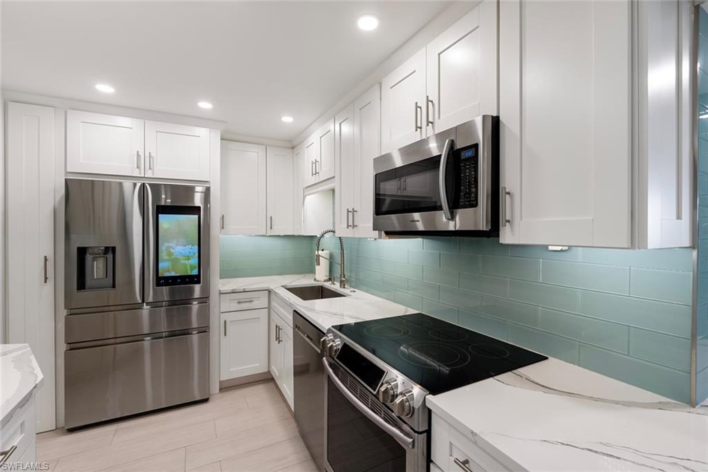 Image 4: Kitchen featuring appliances with stainless steel finishes, white cabinetry, sink, and light stone countertops