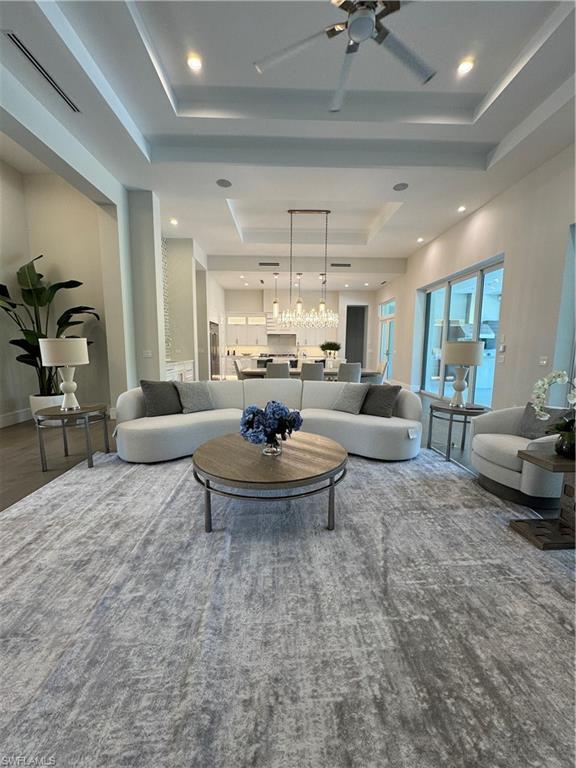Image 2: Living area with a tray ceiling, recessed lighting, ceiling fan with notable chandelier, and visible vents