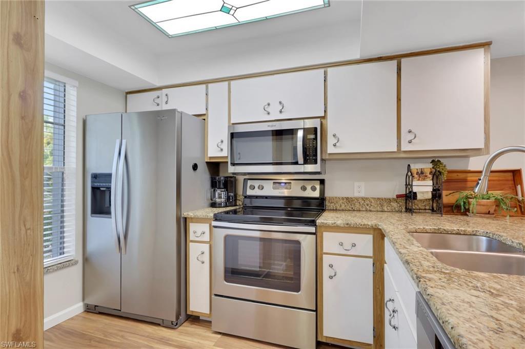 Image 2: Kitchen with stainless steel appliances, white cabinetry, light wood-style flooring, and light stone counters