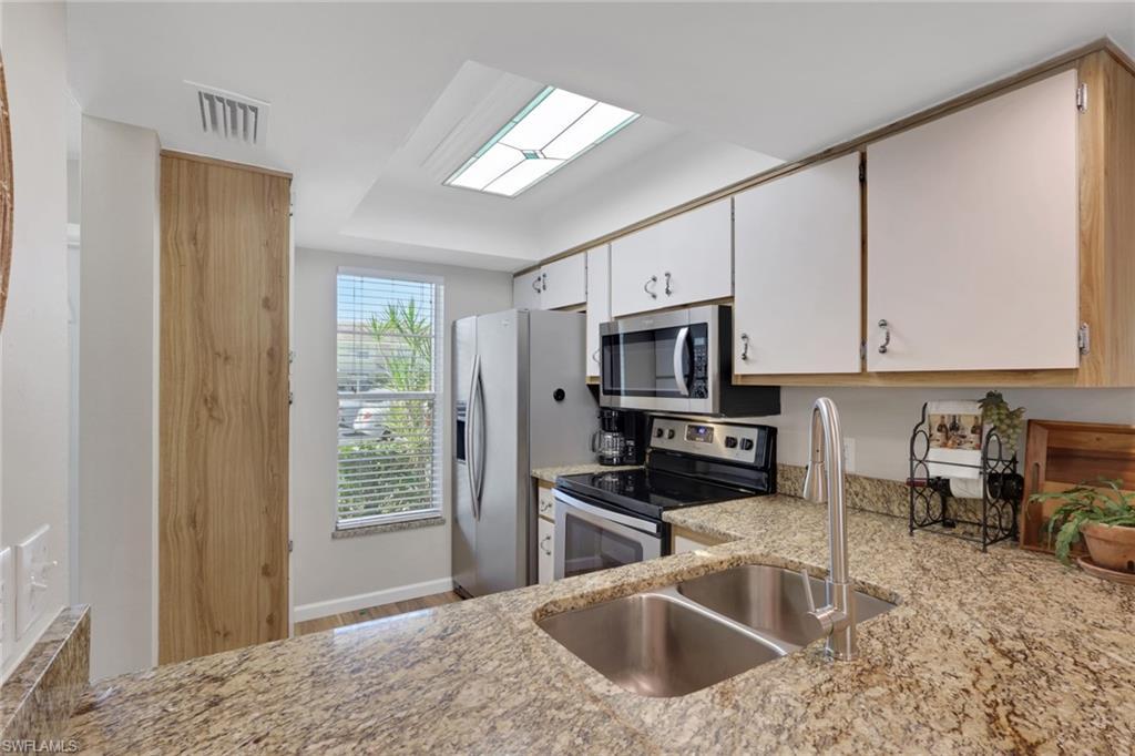 Image 3: Kitchen featuring appliances with stainless steel finishes, white cabinets, light stone countertops, and light wood finished floors