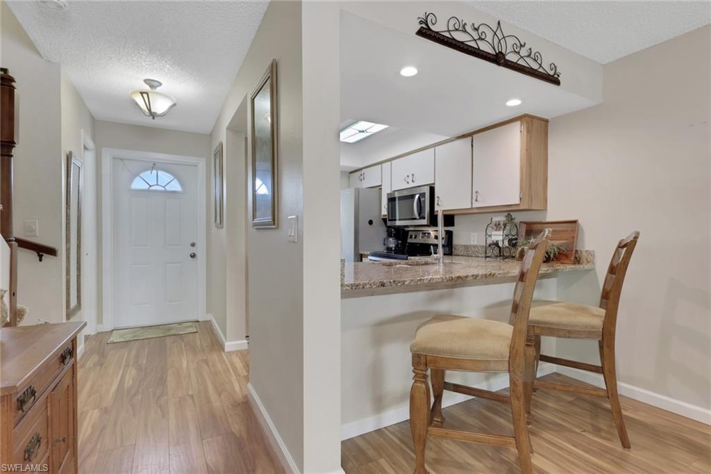 Image 4: Kitchen with a textured ceiling, a kitchen breakfast bar, light wood-style flooring, appliances with stainless steel finishes, and light stone countertops