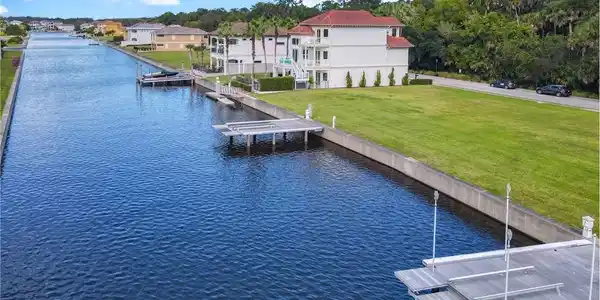 Image 2: Waterfront property featuring a private boat dock with boat lift, canal access, a manicured lawn, and multi-story architectural design
