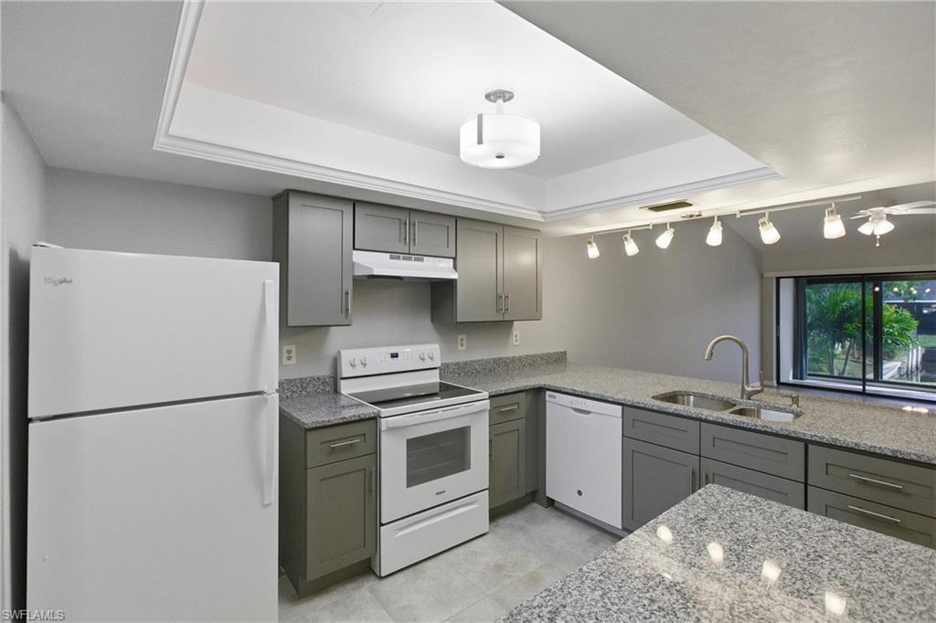 Image 3: Kitchen featuring white appliances, light stone countertops, gray cabinets, a tray ceiling, and under cabinet range hood