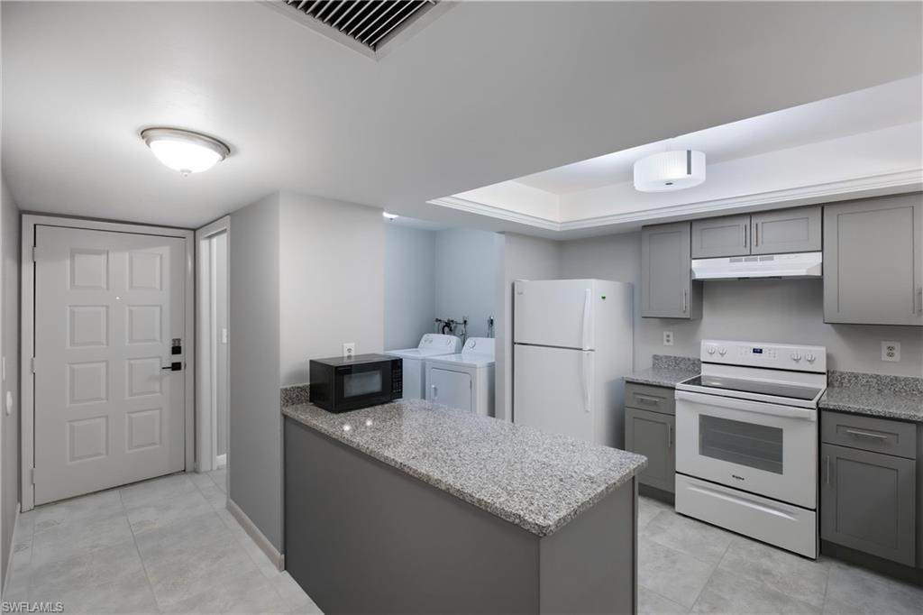 Image 4: Kitchen with gray cabinetry, white appliances, washer and dryer, light stone counters, and a peninsula