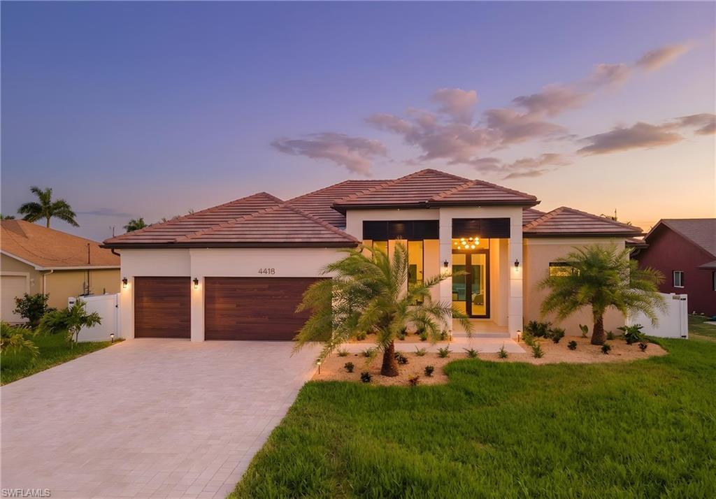 Image 1: Contemporary stucco exterior with a tile roof, paver driveway, and wood-finish garage doors