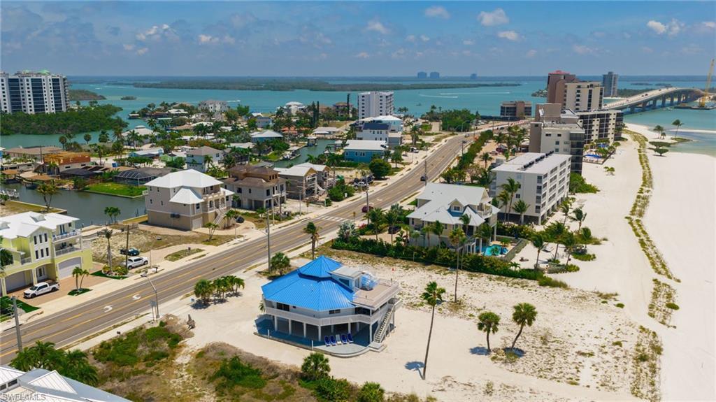 Image 3: Coastal property featuring a vibrant blue roof, multiple balconies, a raised foundation, and palm trees within a beach and canal-front environment - Virtually Edited Image