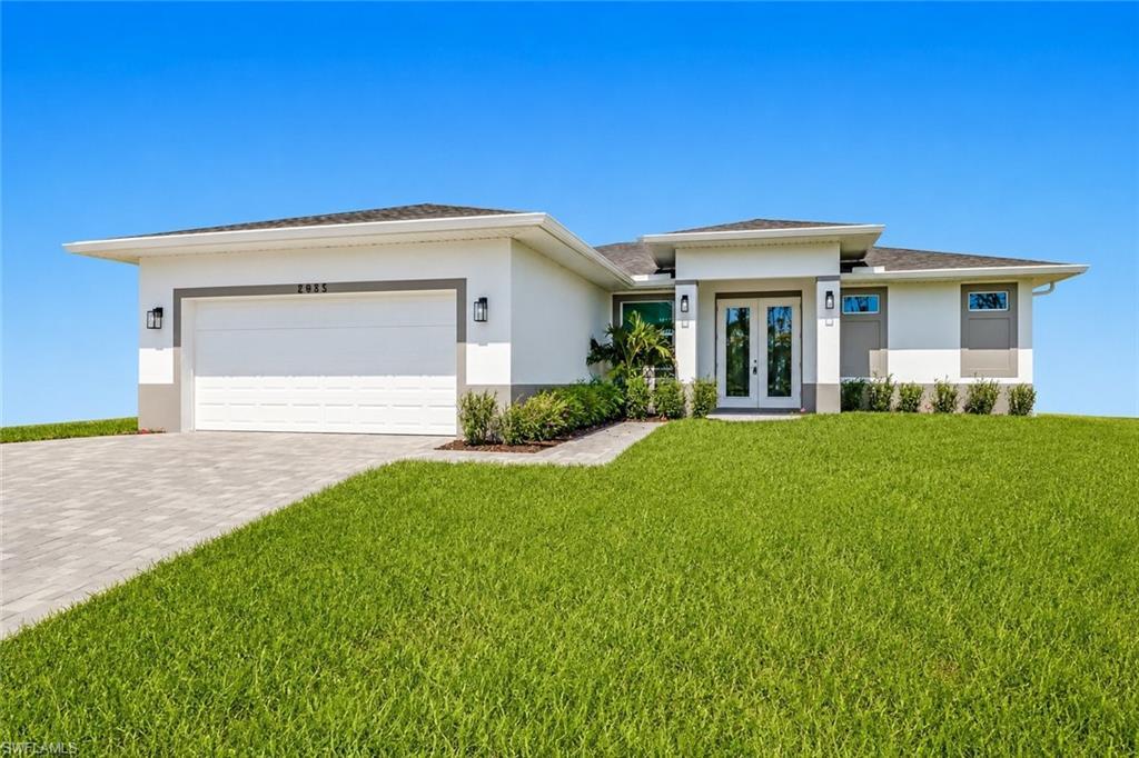 Image 2: Contemporary exterior featuring a white facade with gray accents, a paved driveway, an attached garage, a double-door entry with sidelights, and established landscaping